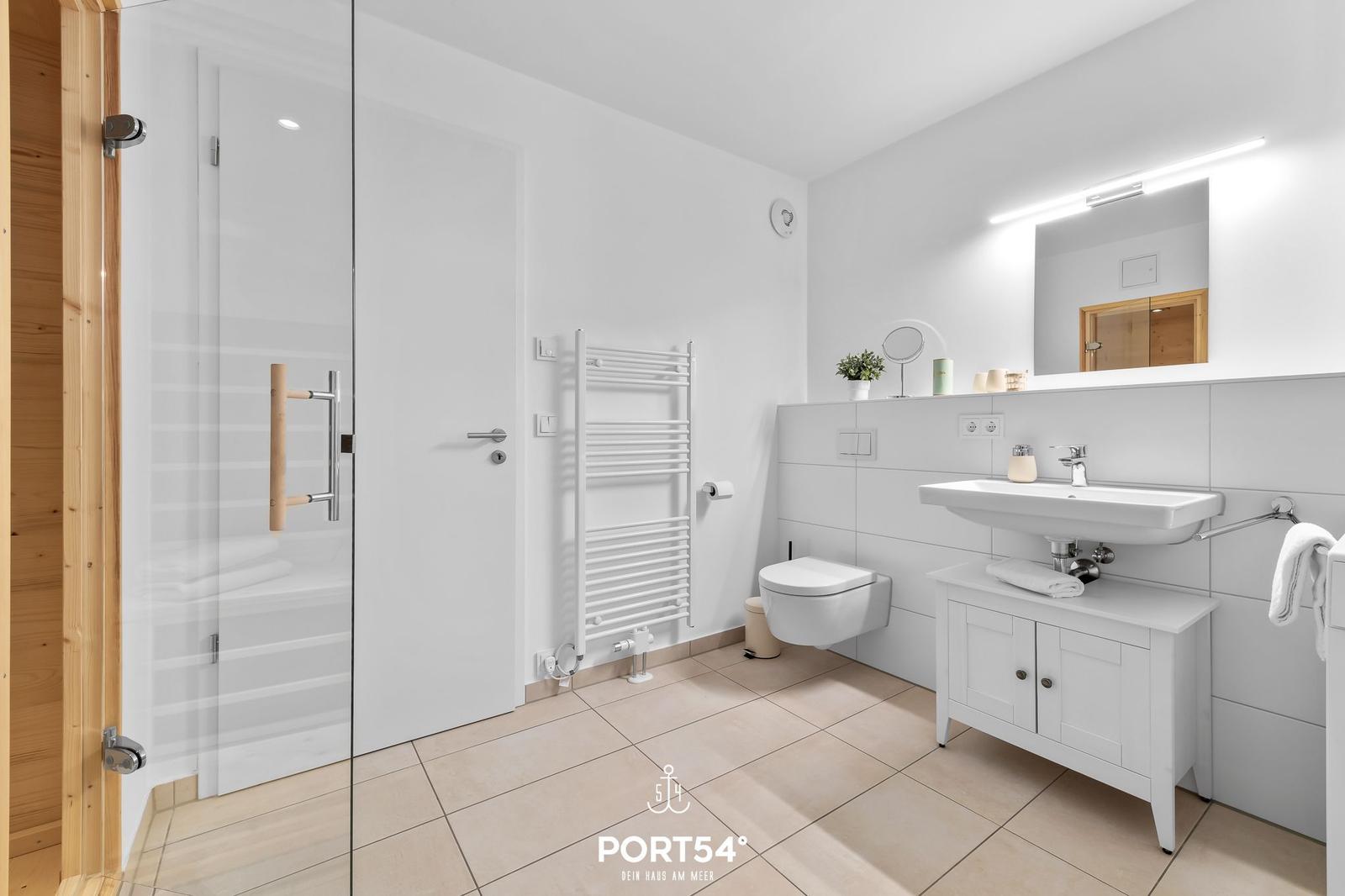 Badezimmer mit Dusche, Waschbecken und Toilette. Weiße Fliesen und Holzelemente.