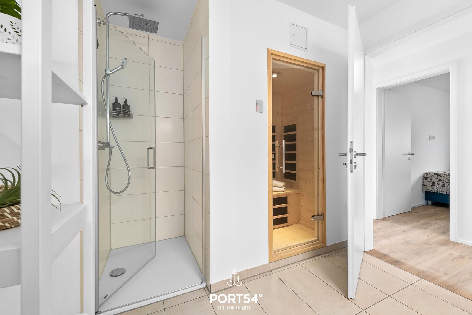 Dusche mit Duschbrause, Sauna und Schlafzimmer im Hintergrund.