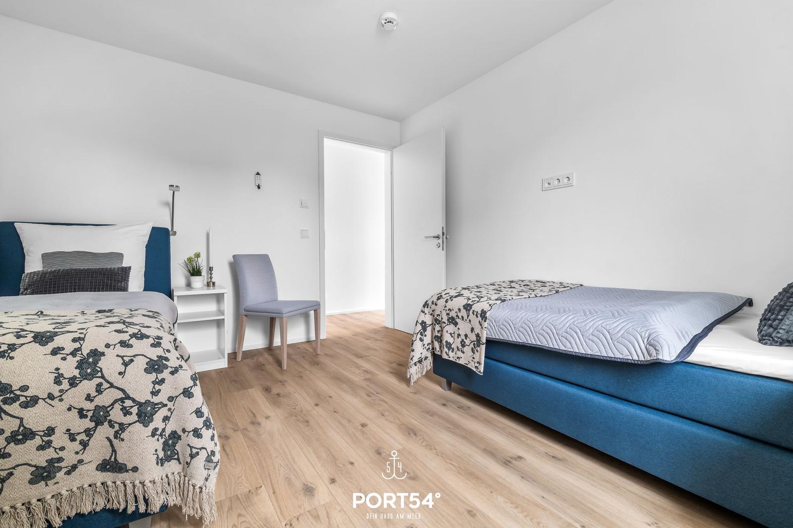 Zwei Betten mit blauen Matratzen und floralen Decken auf Holzboden.