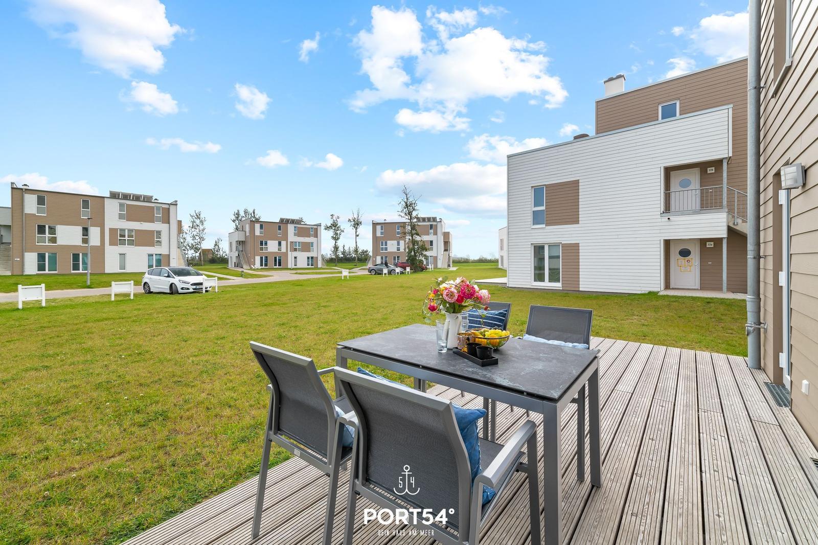 Terrasse mit Tisch und Stühlen, Blick auf moderne Wohnhäuser und Grünfläche.