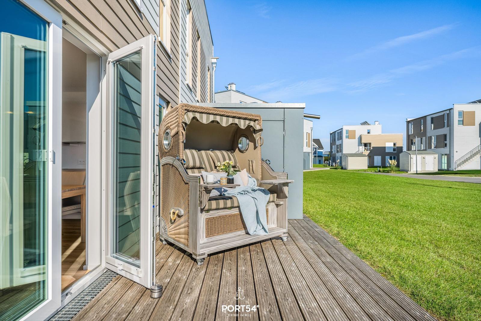 Terrasse mit Strandkorb, Holzdecke und Blick auf Grasflächen und Häuser.