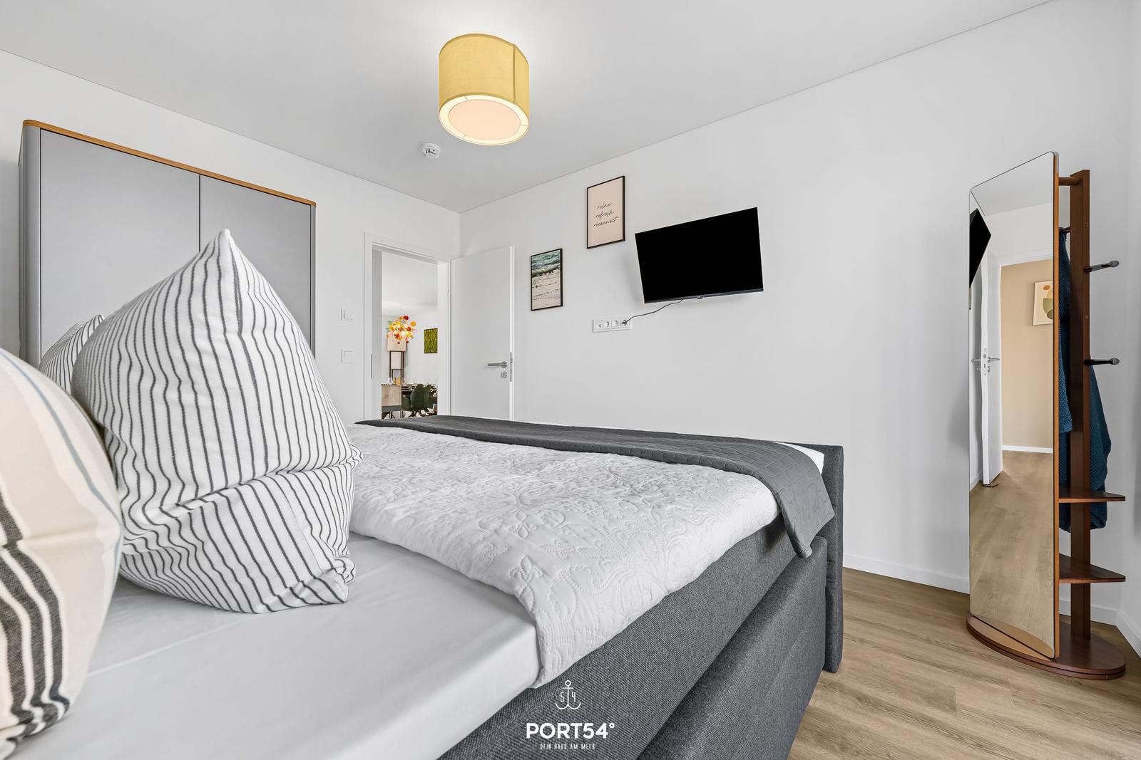 Schlafzimmer mit Bett, Fernseher und Kleiderständer.