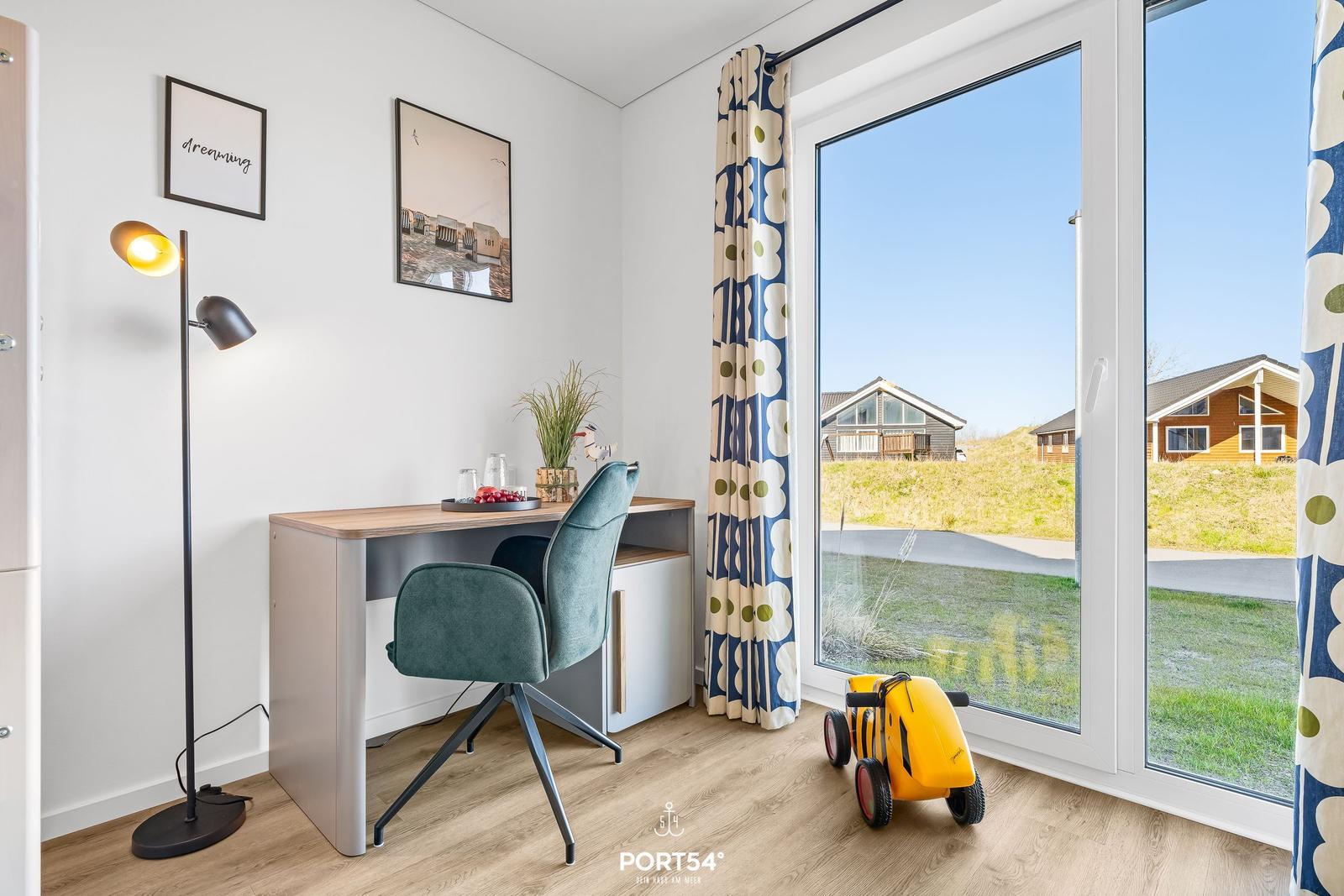 Ein Arbeitszimmer mit Schreibtisch, Stuhl und Fensterblick auf Außenbereich.