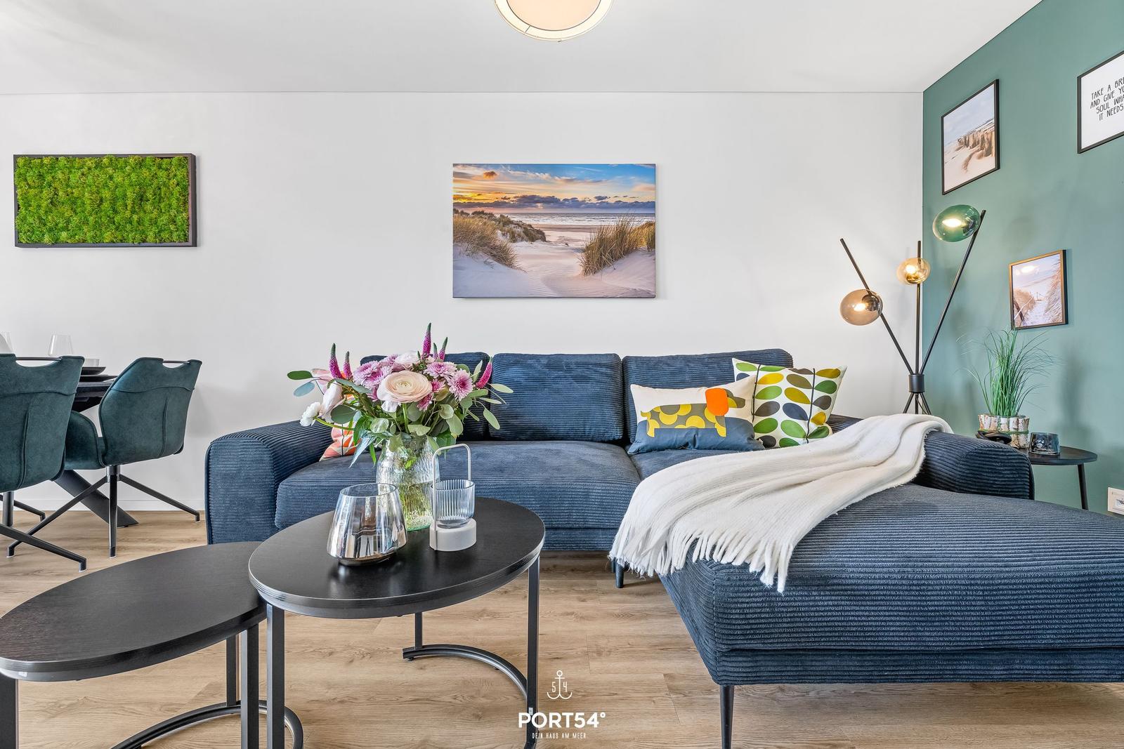 Ein Wohnzimmer mit blauem Sofa, zwei schwarzen Tischen und Wandbildern.