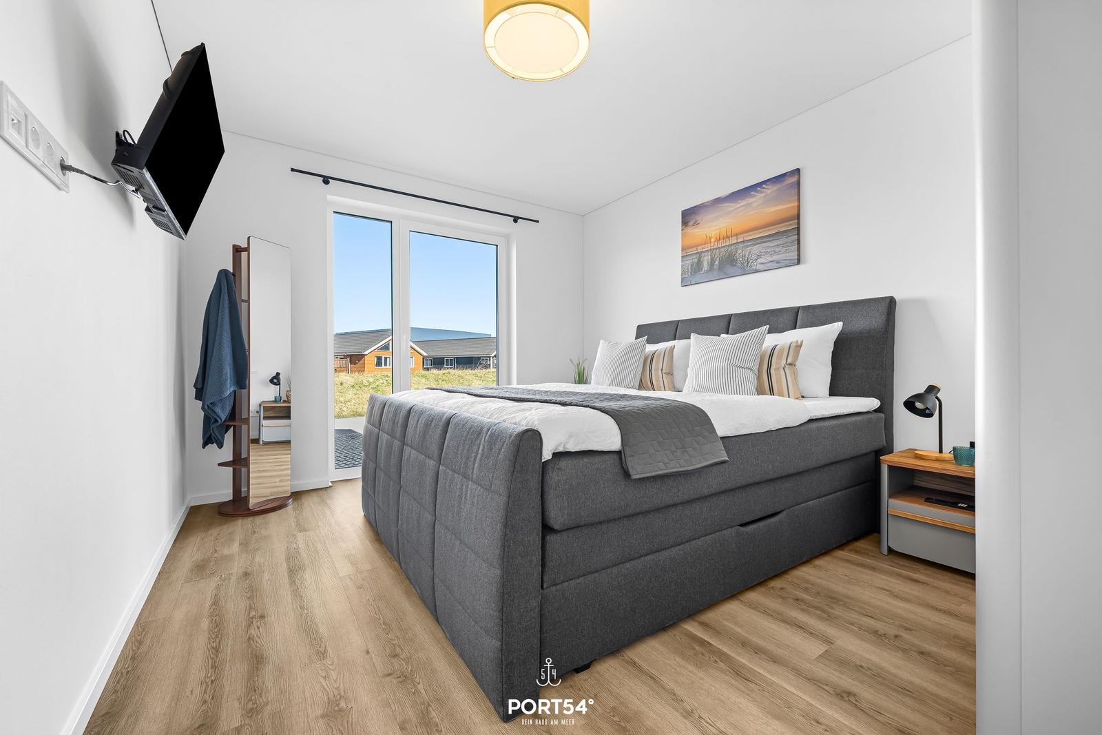 Schlafzimmer mit Bett, TV und Fensterblick auf Außenbereich.