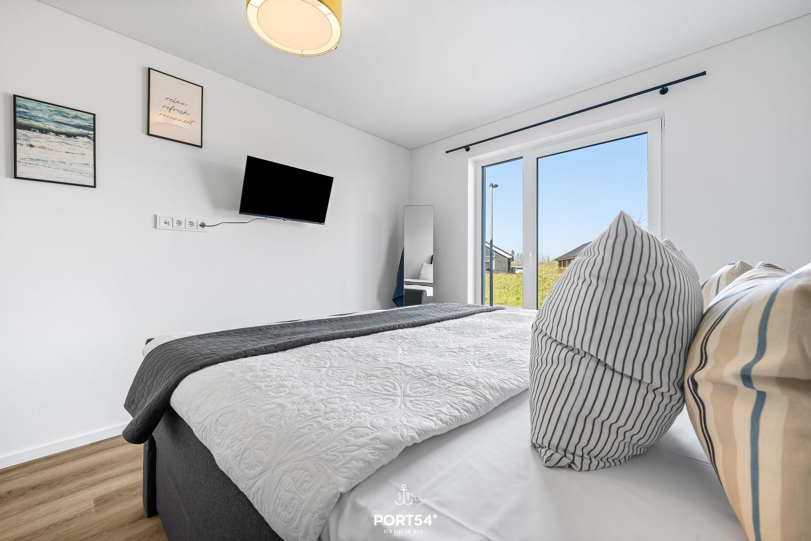 Schlafzimmer mit Bett, TV und Fenster. Wandbild und Deckenleuchte sichtbar.