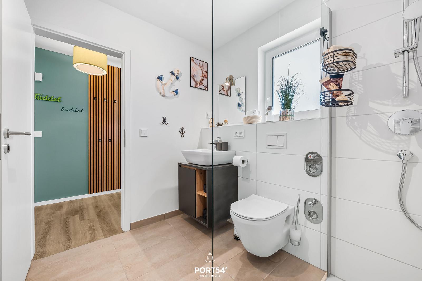 Badezimmer mit Dusche, Waschbecken und Toilette. Sehenswert: Ankerdekoration und Fenster mit Pflanze.
