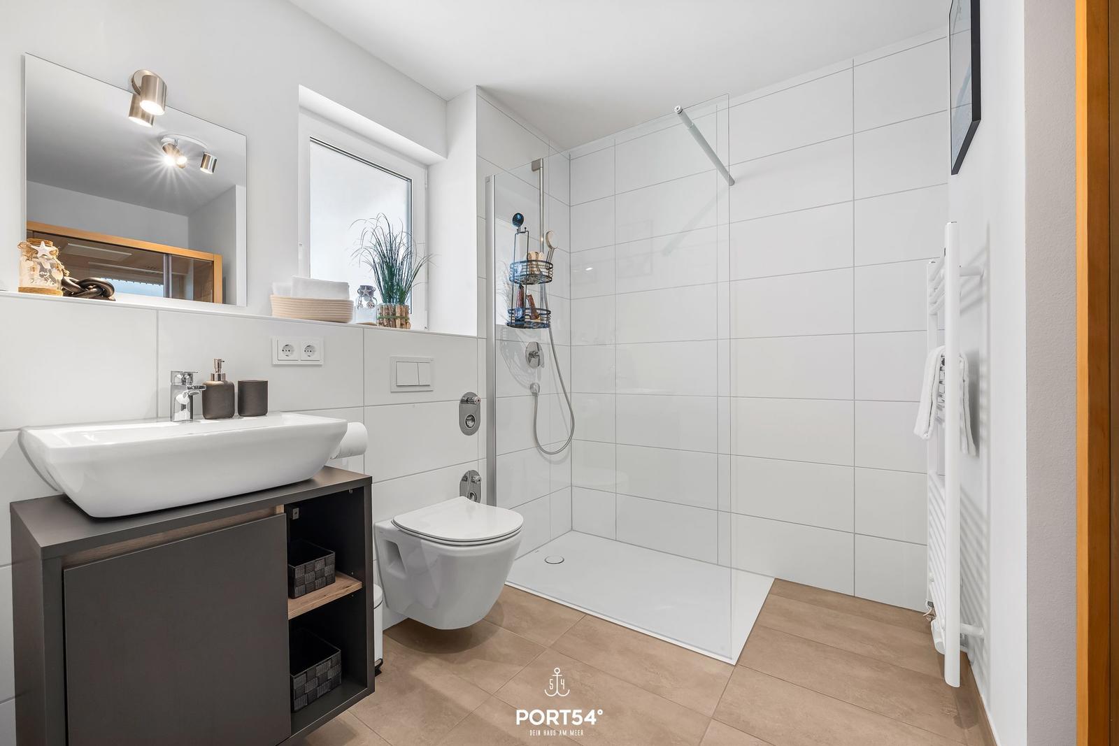 Badezimmer mit Dusche, Waschbecken und Toilette. Weiße Fliesen und Holzboden.
