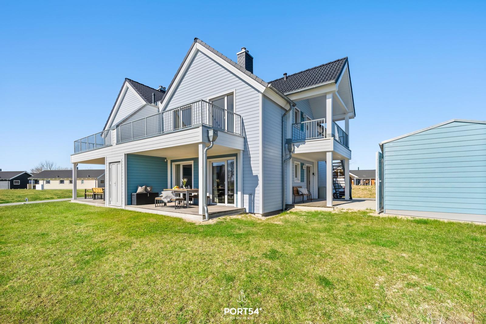 Zweistöckiges Haus mit Balkon und Terrasse auf grünem Grundstück.