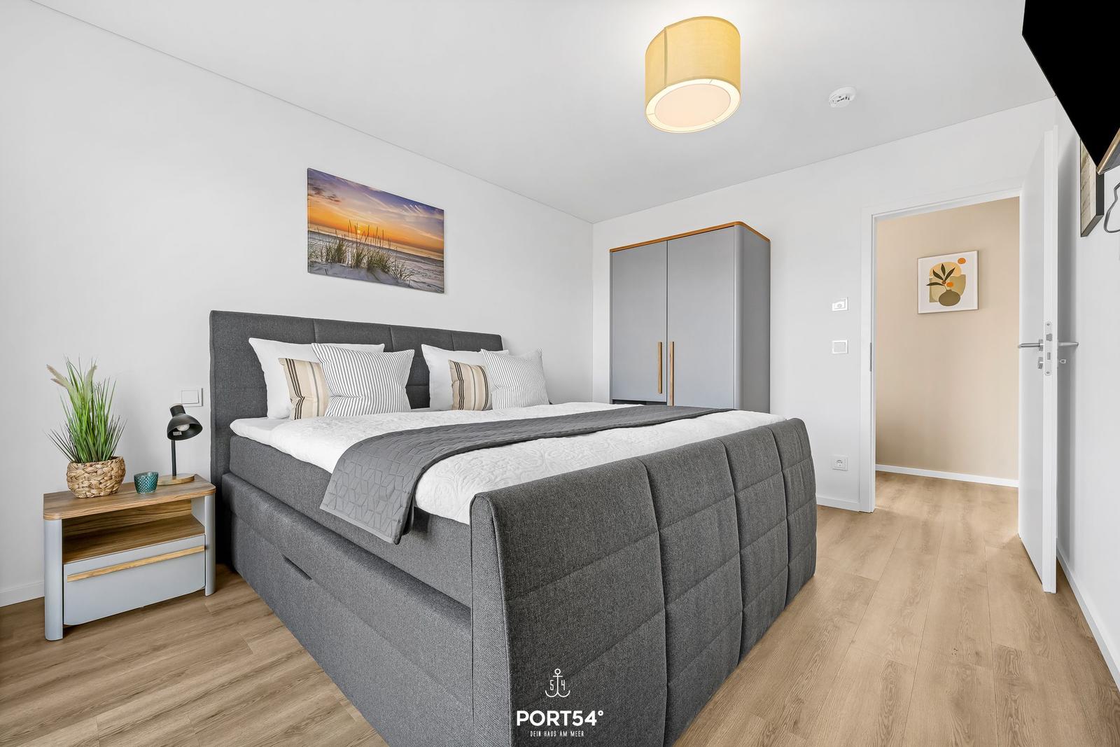 Schlafzimmer mit Doppelbett, Nachttisch, Kleiderschrank und Wandbild.