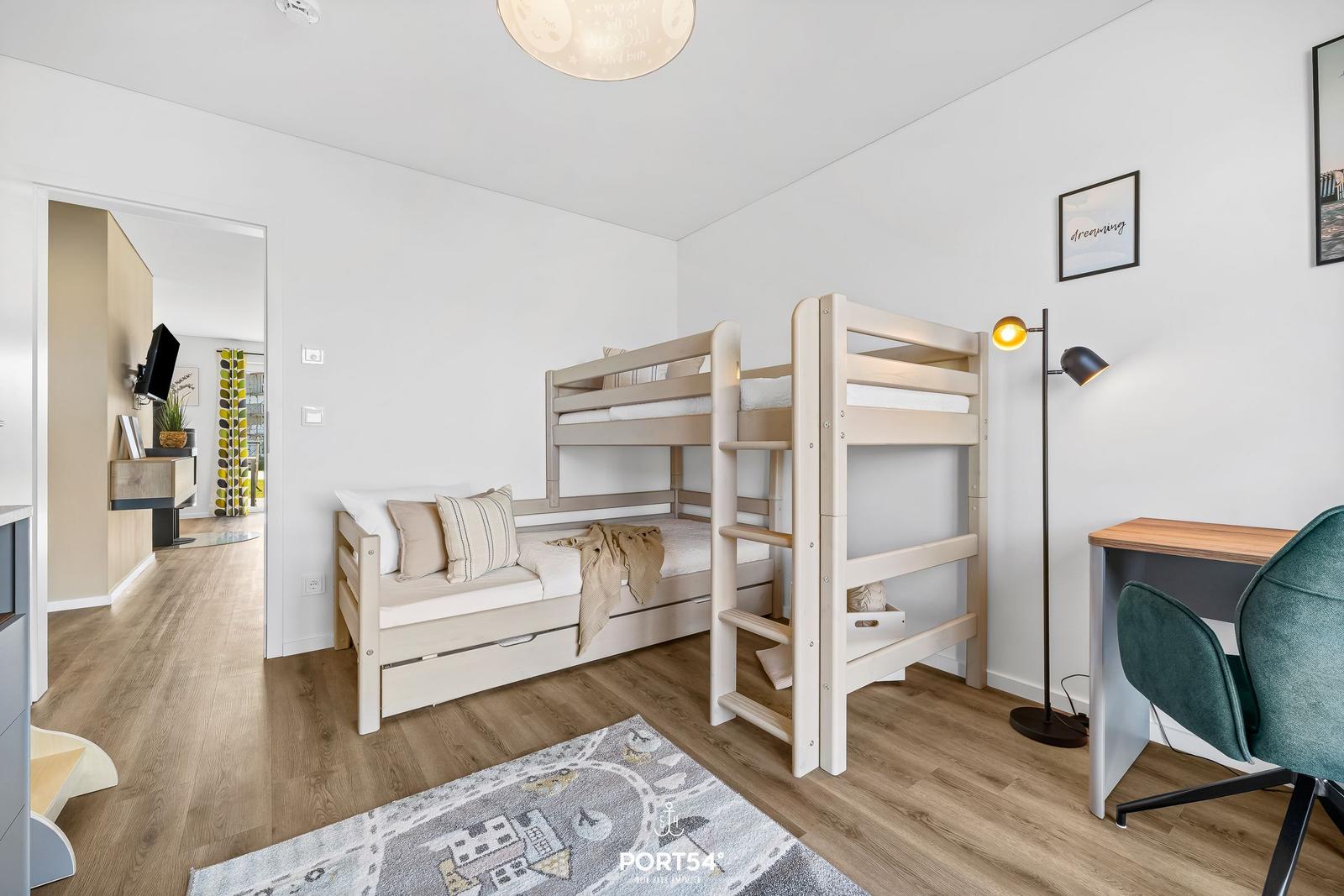 Zimmer mit Doppelstockbett, Schreibtisch und Stehlampe. Holzboden und Wandbilder.