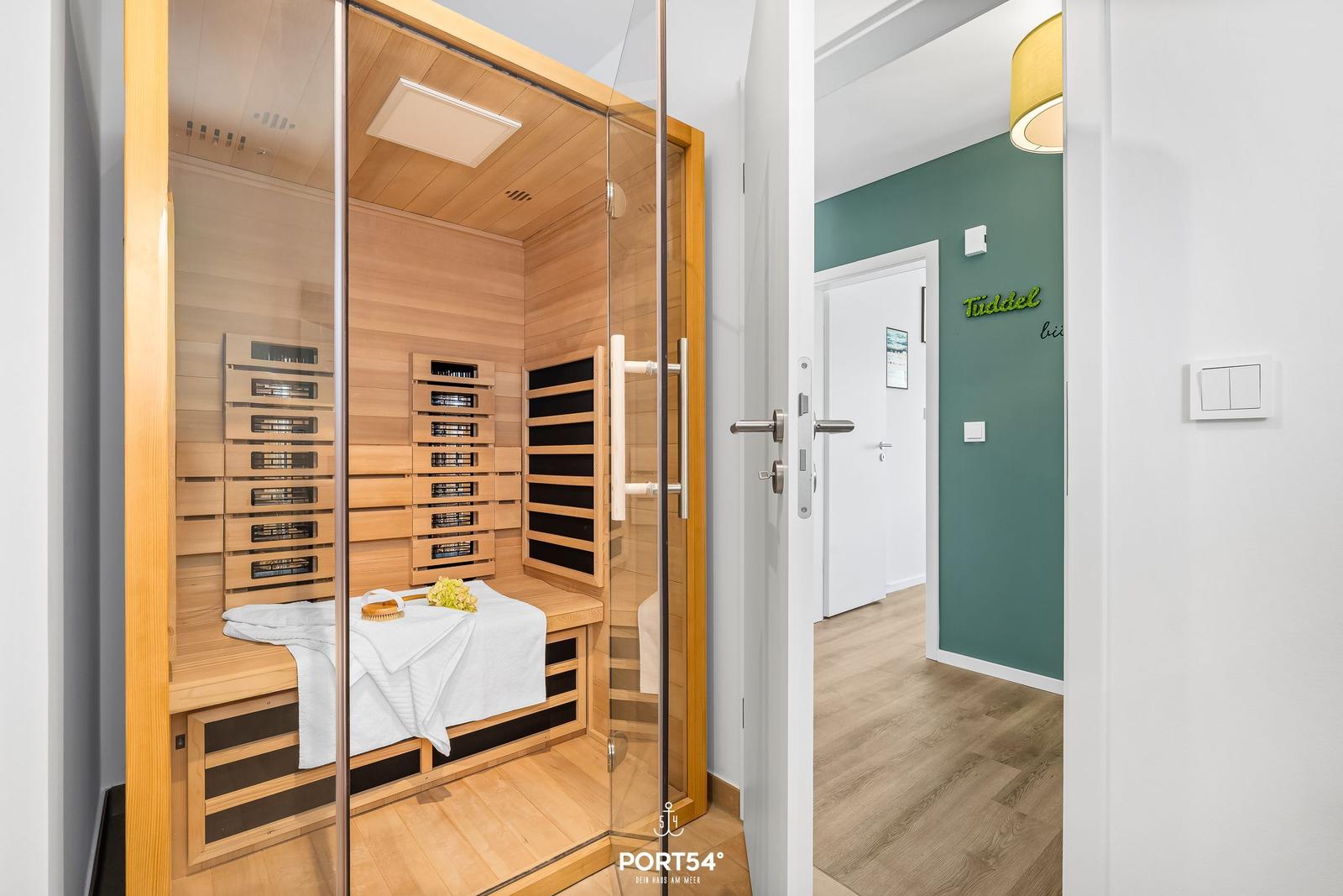 Sauna mit Holzwand und Liegefläche. Tür führt in Flur mit grüner Wand.
