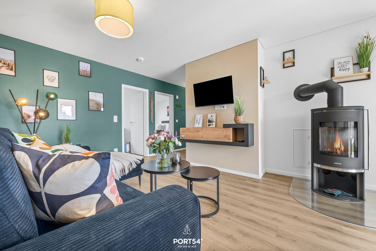 Wohnzimmer mit Sofa, Kamin und Wandfernseher. Grüne Wand mit Bildern und Holzboden.