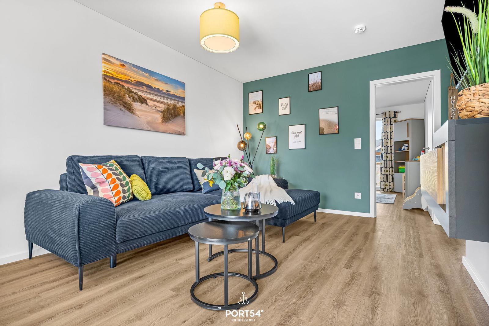 Ein Wohnzimmer mit blauem Sofa, Holzboden und grüner Wand mit Bildern.