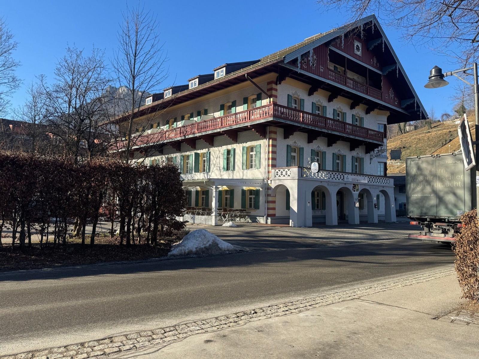 Ein großes Gebäude mit Balkonen und grünen Fensterläden. Hinterhof mit Schnee und Bäumen.