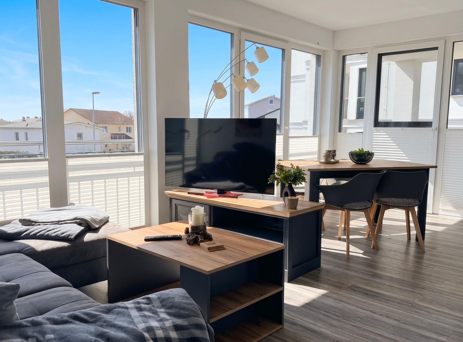 Wohnzimmer mit TV, Esstisch und großem Fensterblick auf Balkon.