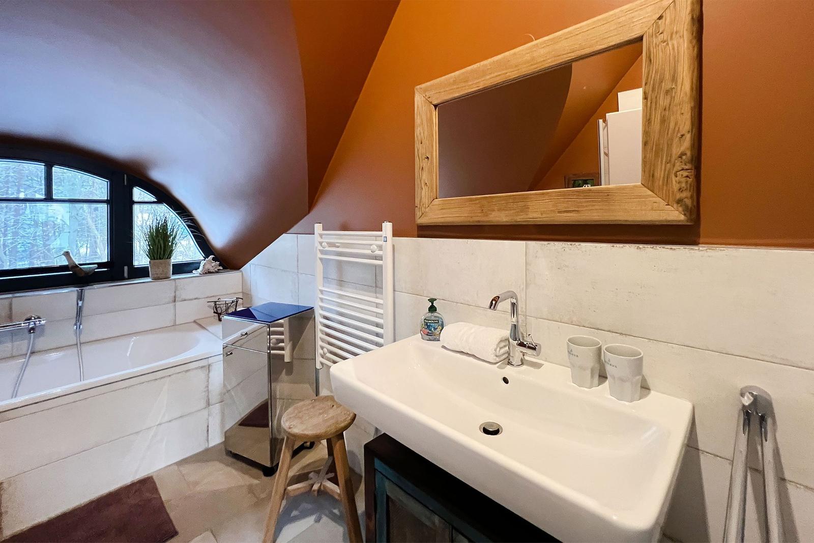 Badezimmer mit Badewanne, Waschbecken und Spiegel an schräger Wand.