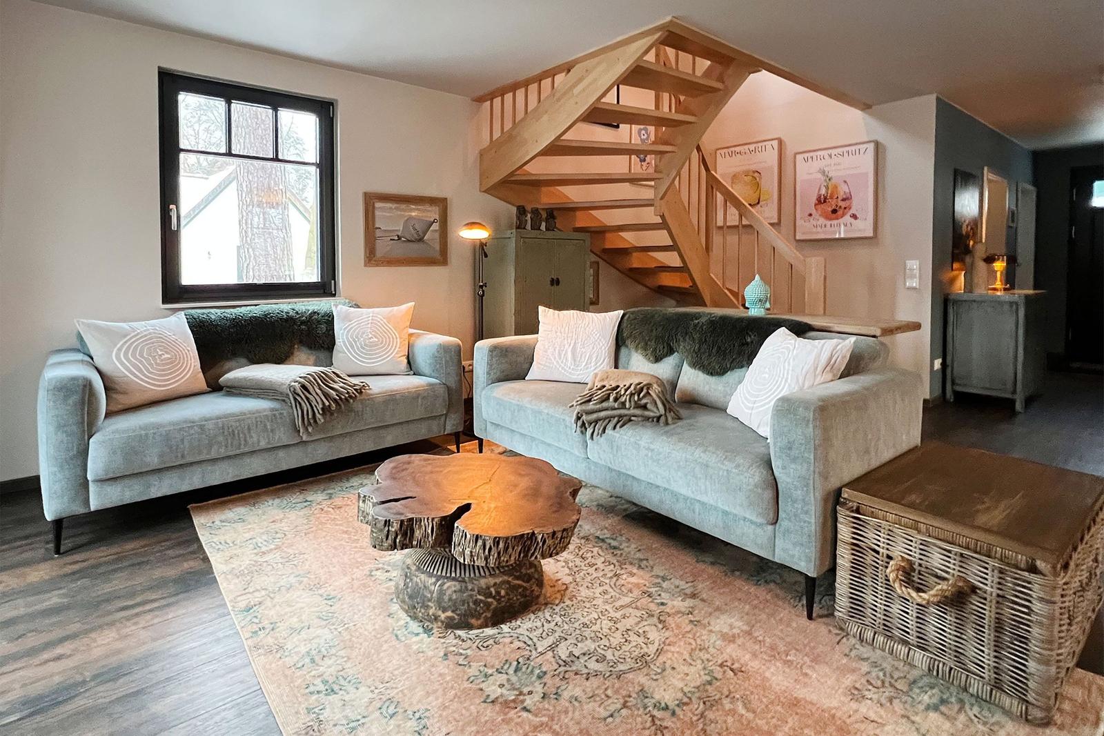 Zwei Sofas mit Kissen und Decken stehen auf einem Teppich. Eine Holztreppe führt zur oberen Etage.