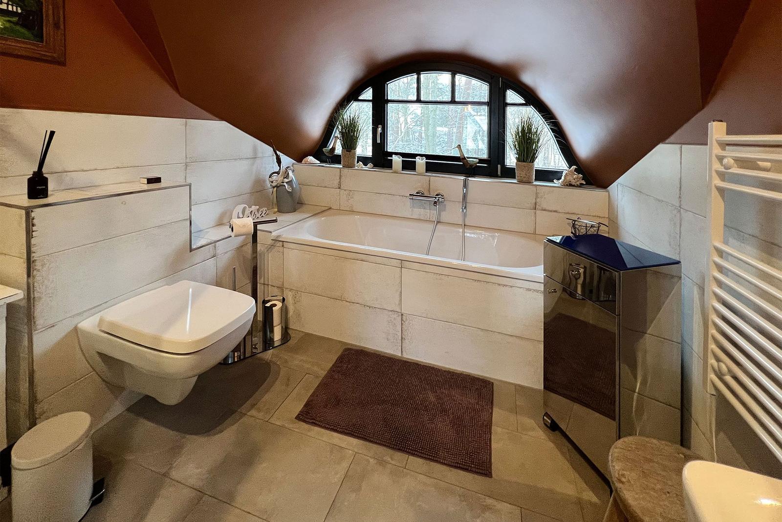 Bad mit Badewanne, Toilette und Fenster mit Blick auf Wald.