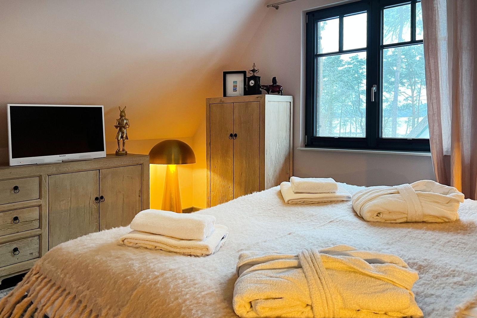 Schlafzimmer mit Bett, Fernseher und Fenster mit Blick auf Wald.