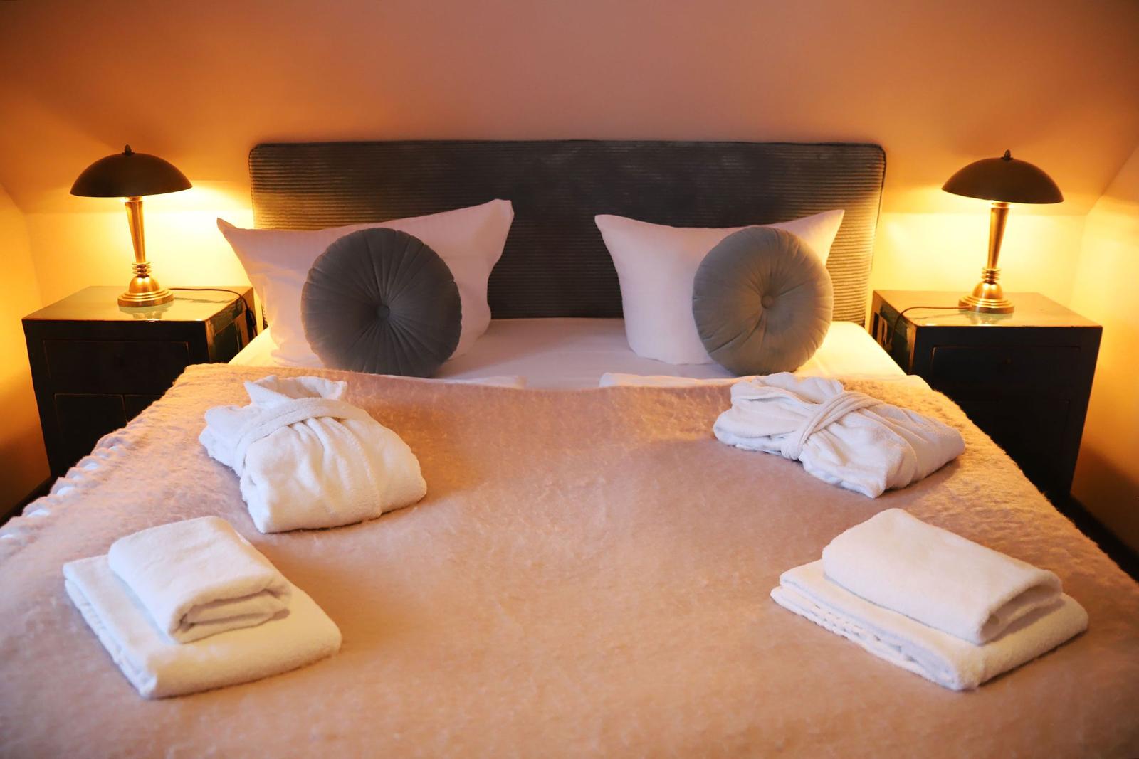 Doppelbett mit Kissen, Bademänteln und Handtüchern. Zwei Nachttische mit Lampen.