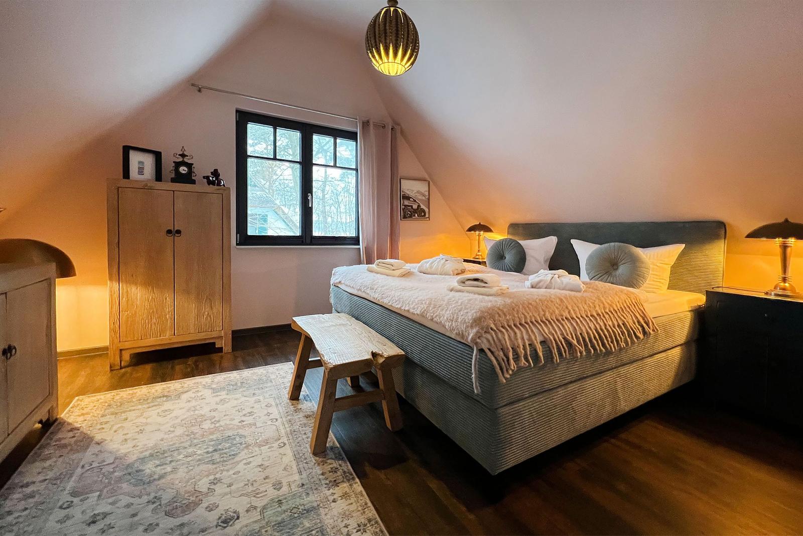 Schlafzimmer mit Bett, Schrank und Fenster. Holzboden und Teppich.