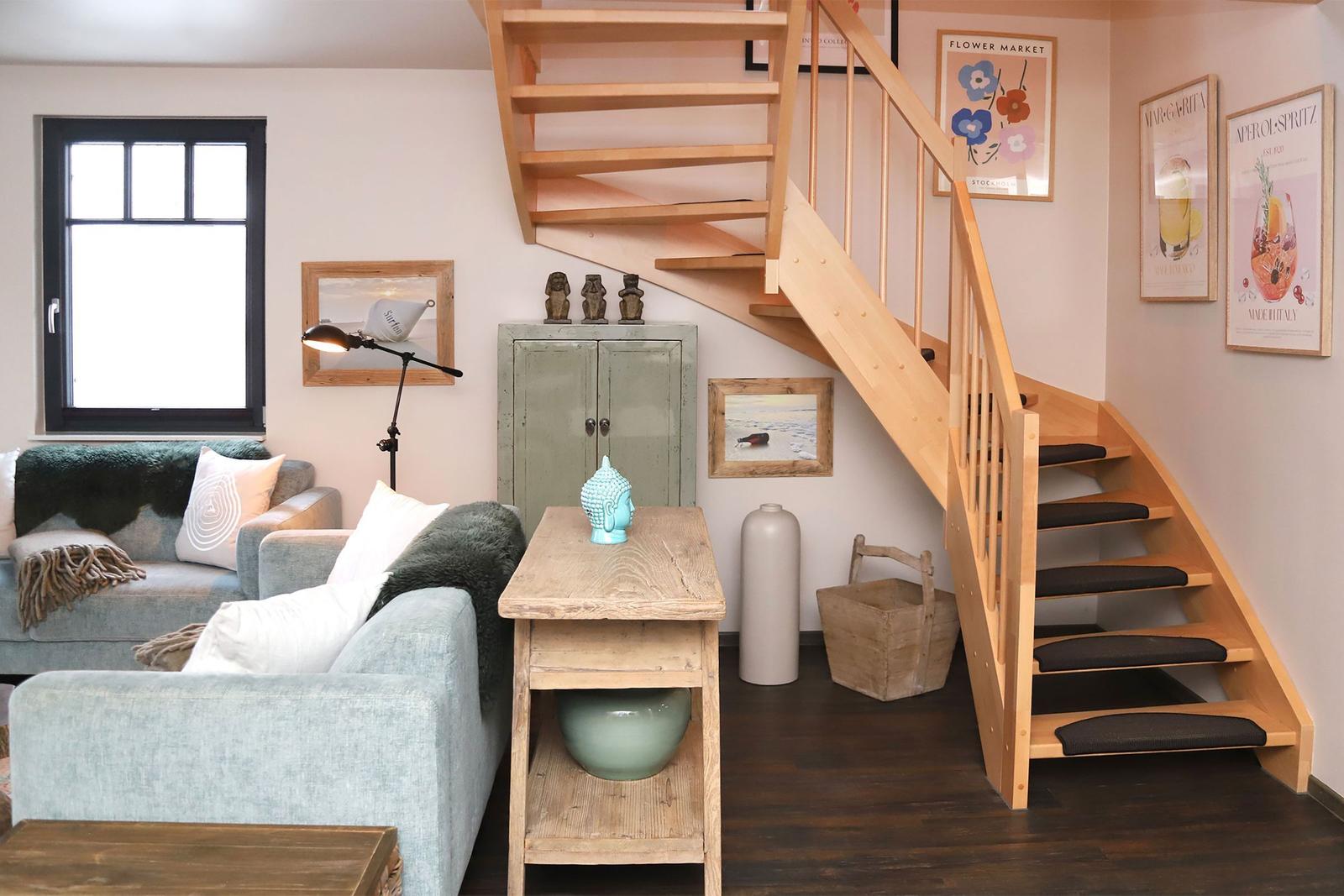 Wohnzimmer mit Holztreppe, Sofa, Tisch und Wandbildern.