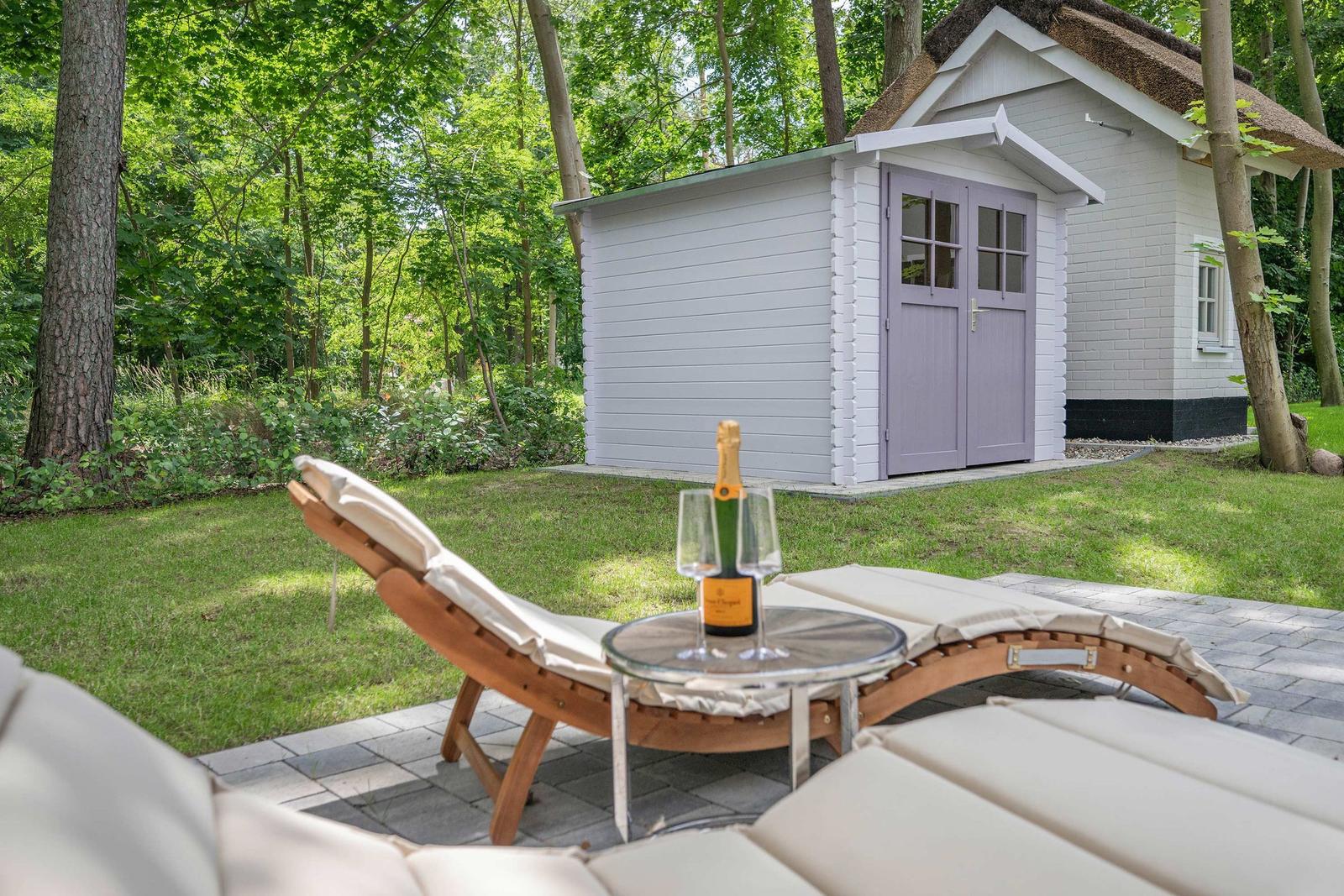 Außenbereich mit Liegestühlen und einem Tisch mit Champagner. Im Hintergrund ein kleines Haus mit Dach aus Stroh.
