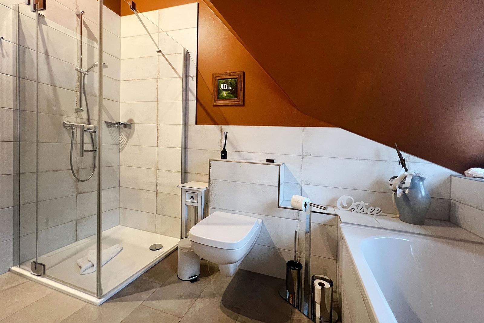 Badezimmer mit Dusche, Toilette und Badewanne unter schräger Decke.