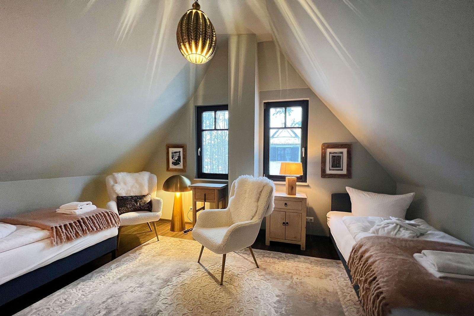 Zimmer mit zwei Betten, zwei Sesseln und Fenstern mit Blick nach draußen.