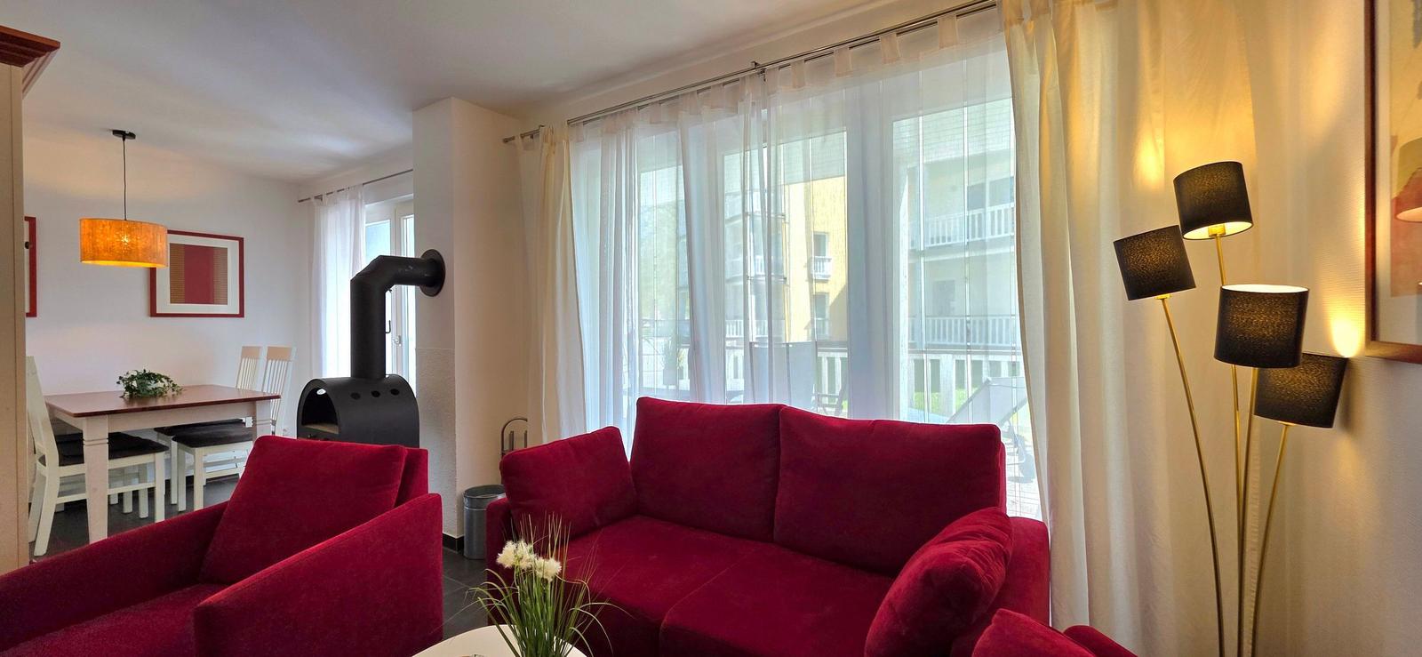 Wohnzimmer mit rotem Sofa, Essbereich und Fenster mit Blick auf Gebäude
