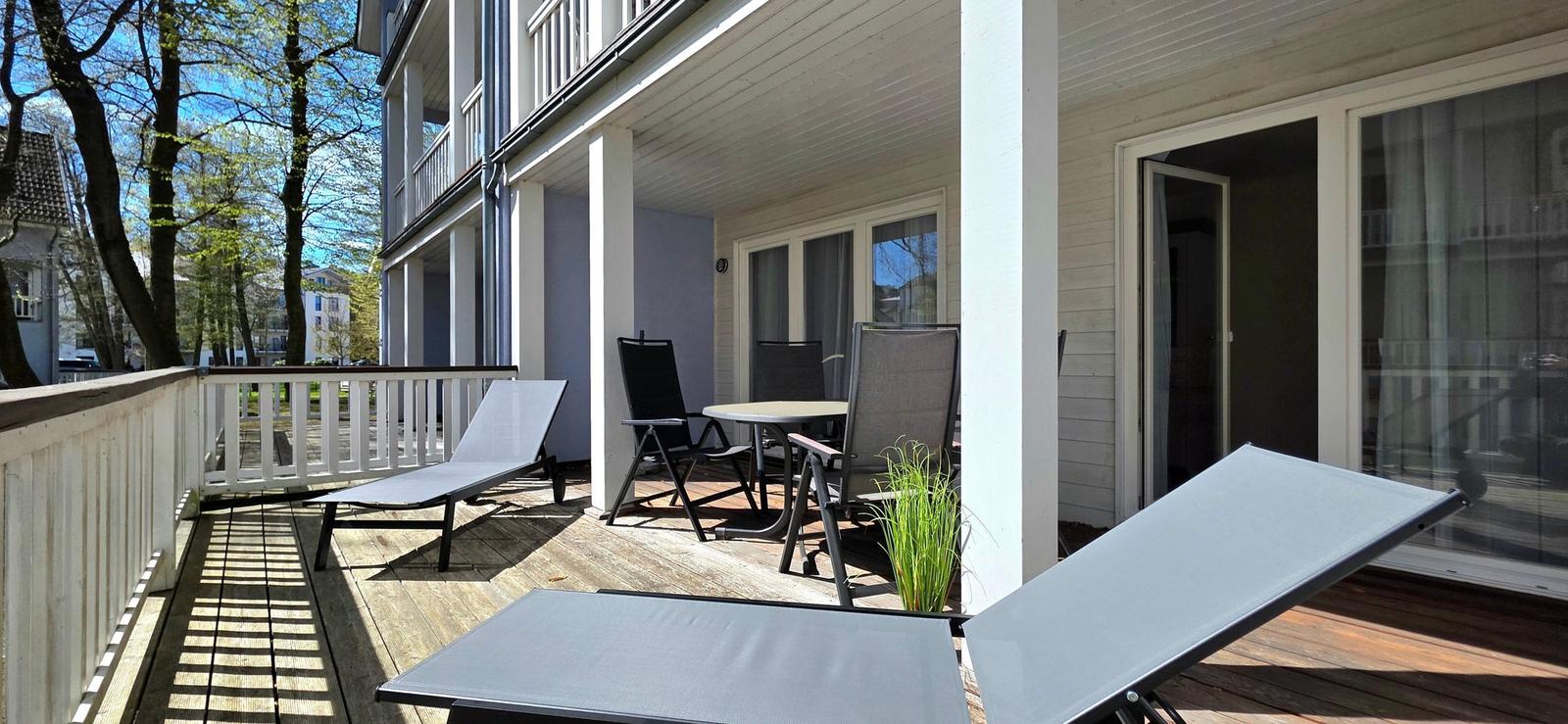 Terrasse mit Liegestühlen, Tisch und Stühlen. Holzdeck und Sicht auf Bäume.