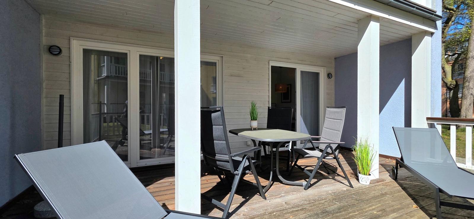 Terrasse mit Tisch, Stühlen und Liegestühlen. Holzdecke und weiße Säulen.