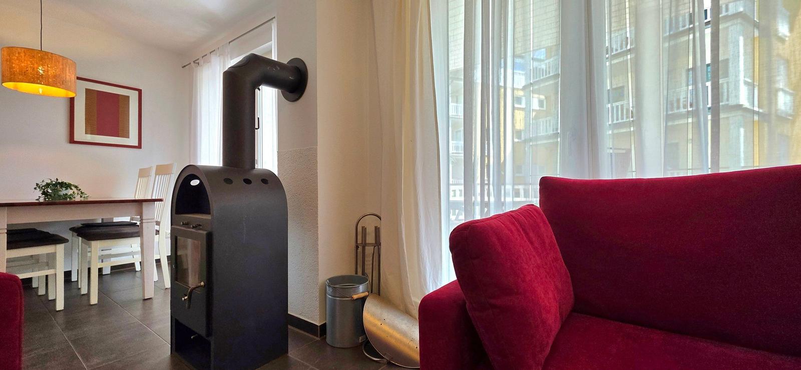 Ein Wohnzimmer mit rotem Sofa, Holztisch, Stühlen und einem Kaminofen.