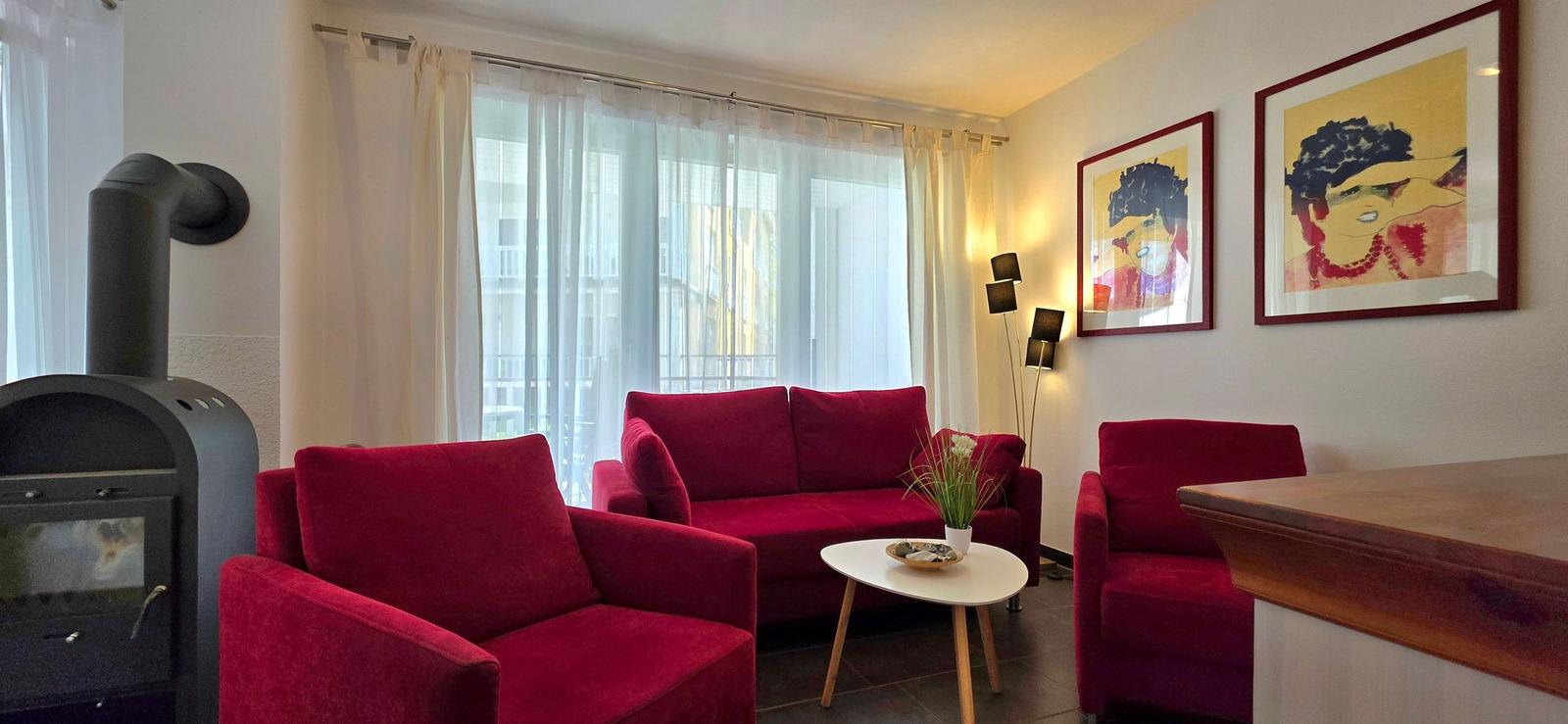 Ein Wohnzimmer mit roten Sesseln, einem Sofa und einem Kaminofen.
