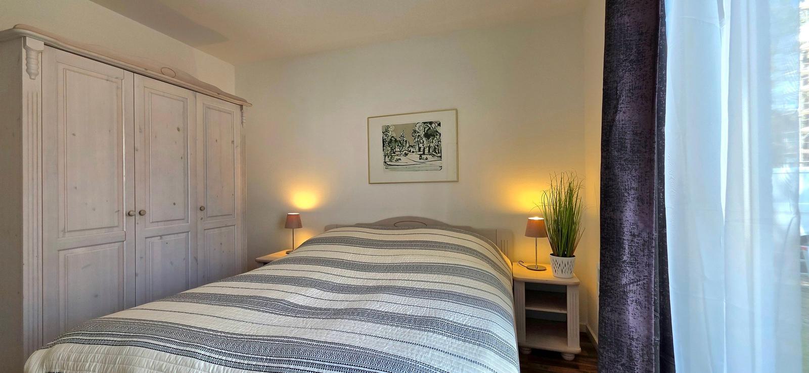 Schlafzimmer mit Bett, Kleiderschrank und Nachttischen mit Lampen.