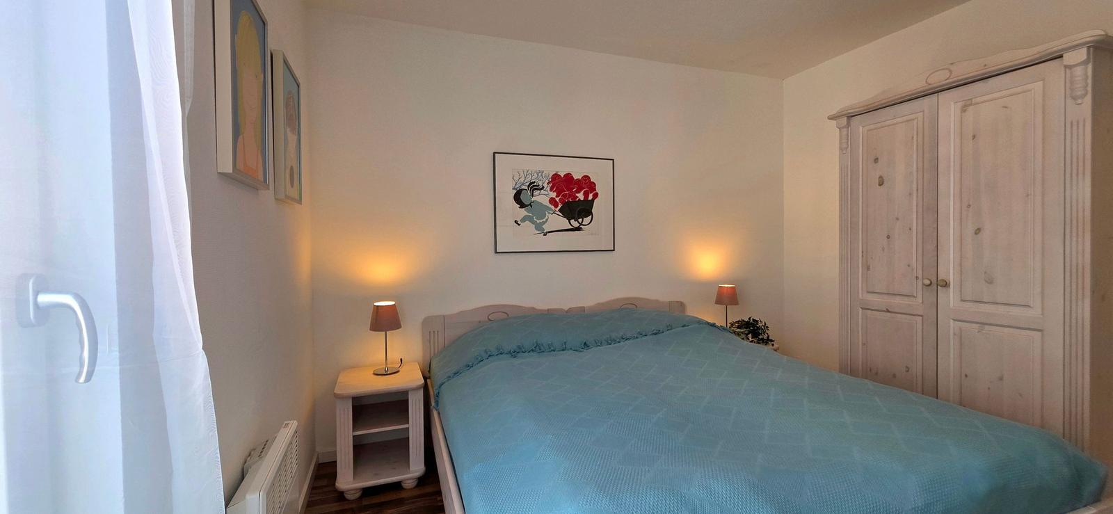 Schlafzimmer mit Bett, Kleiderschrank und Nachttisch mit Lampen.