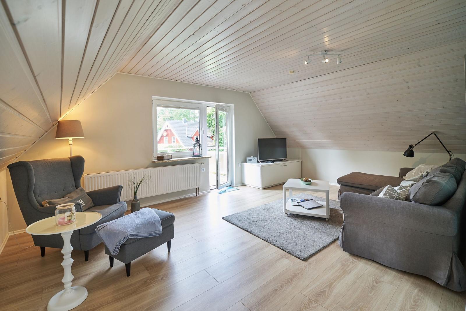 Wohnzimmer mit Sofa, Sessel und TV. Holzdecke und Terrassentür.