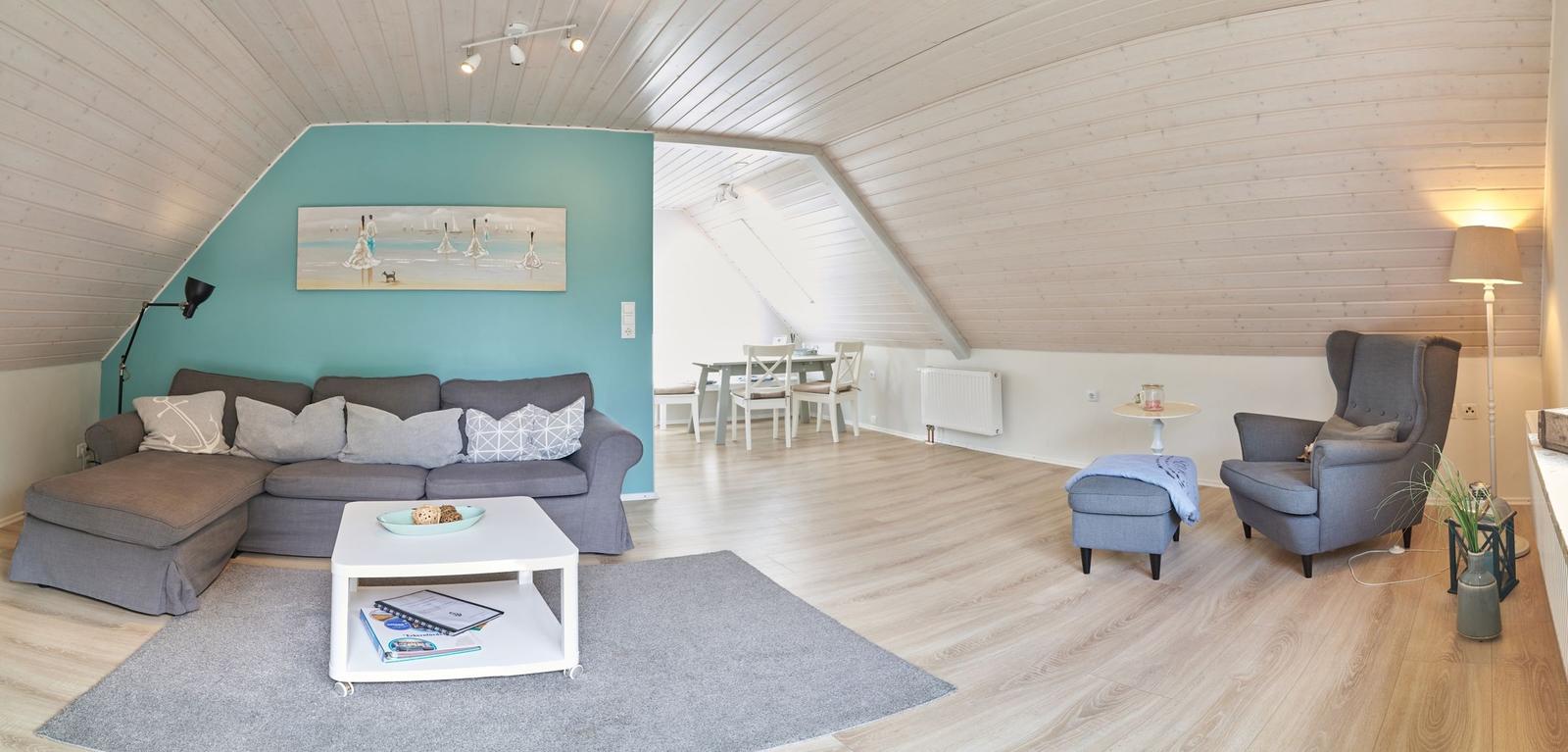 Wohn- und Essbereich mit Sofa, Sessel und Holzboden unter schrägen Dachschrägen.