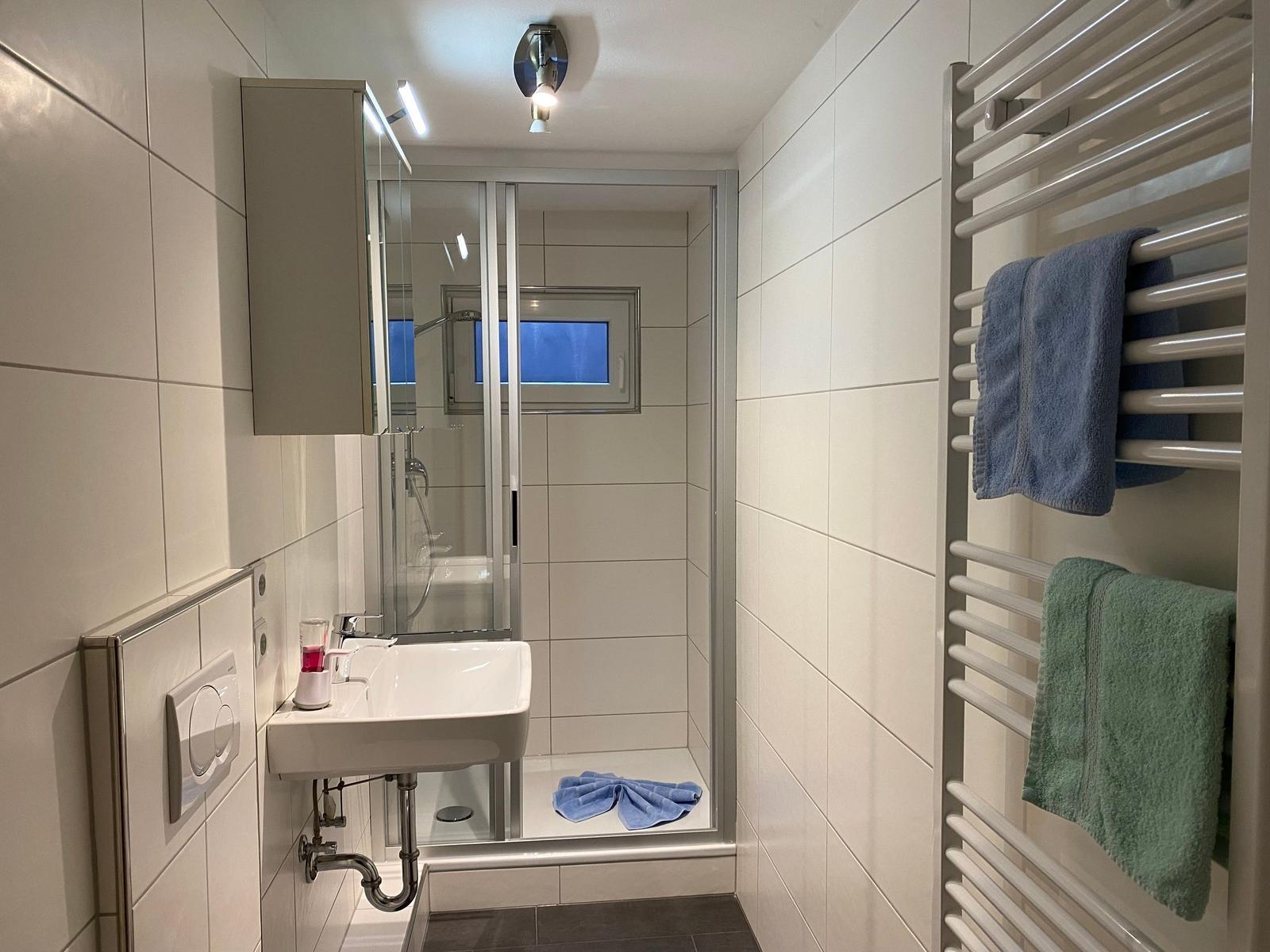 Badezimmer mit Dusche, Waschbecken und Heizkörper mit Handtüchern.