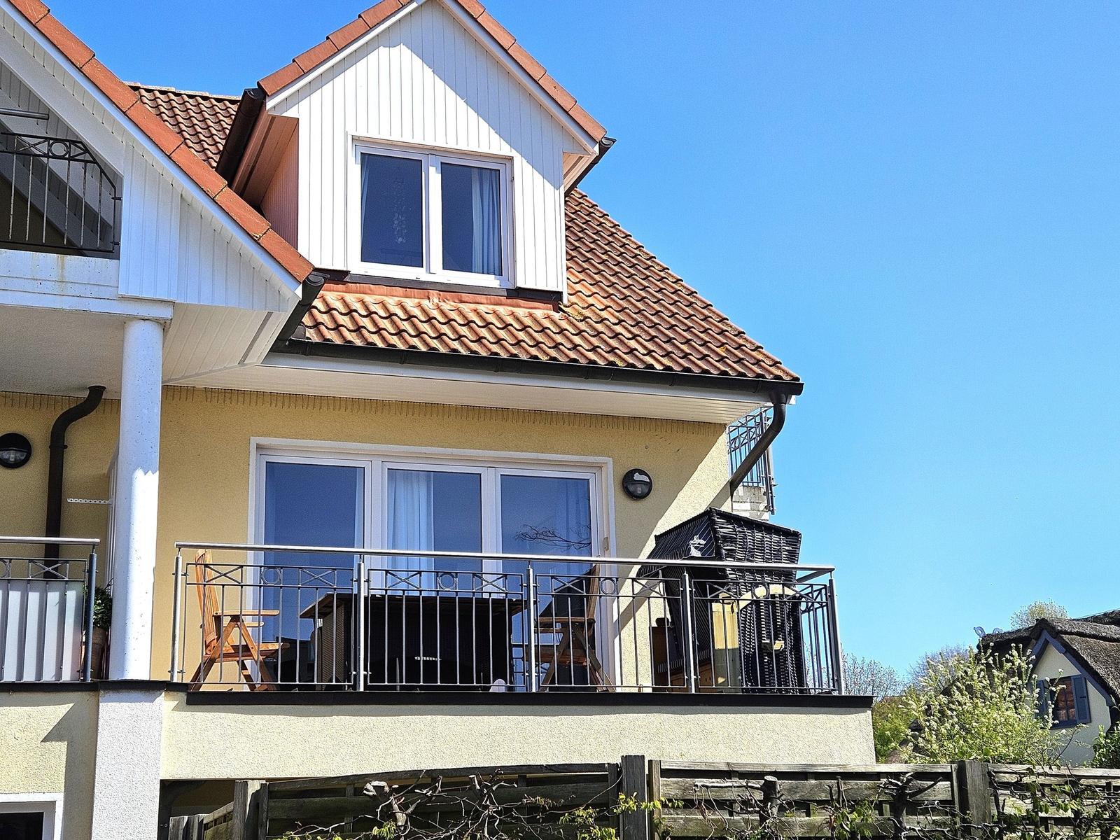 Haus mit Balkon, Dachterrasse und rotem Ziegeldach unter blauem Himmel.