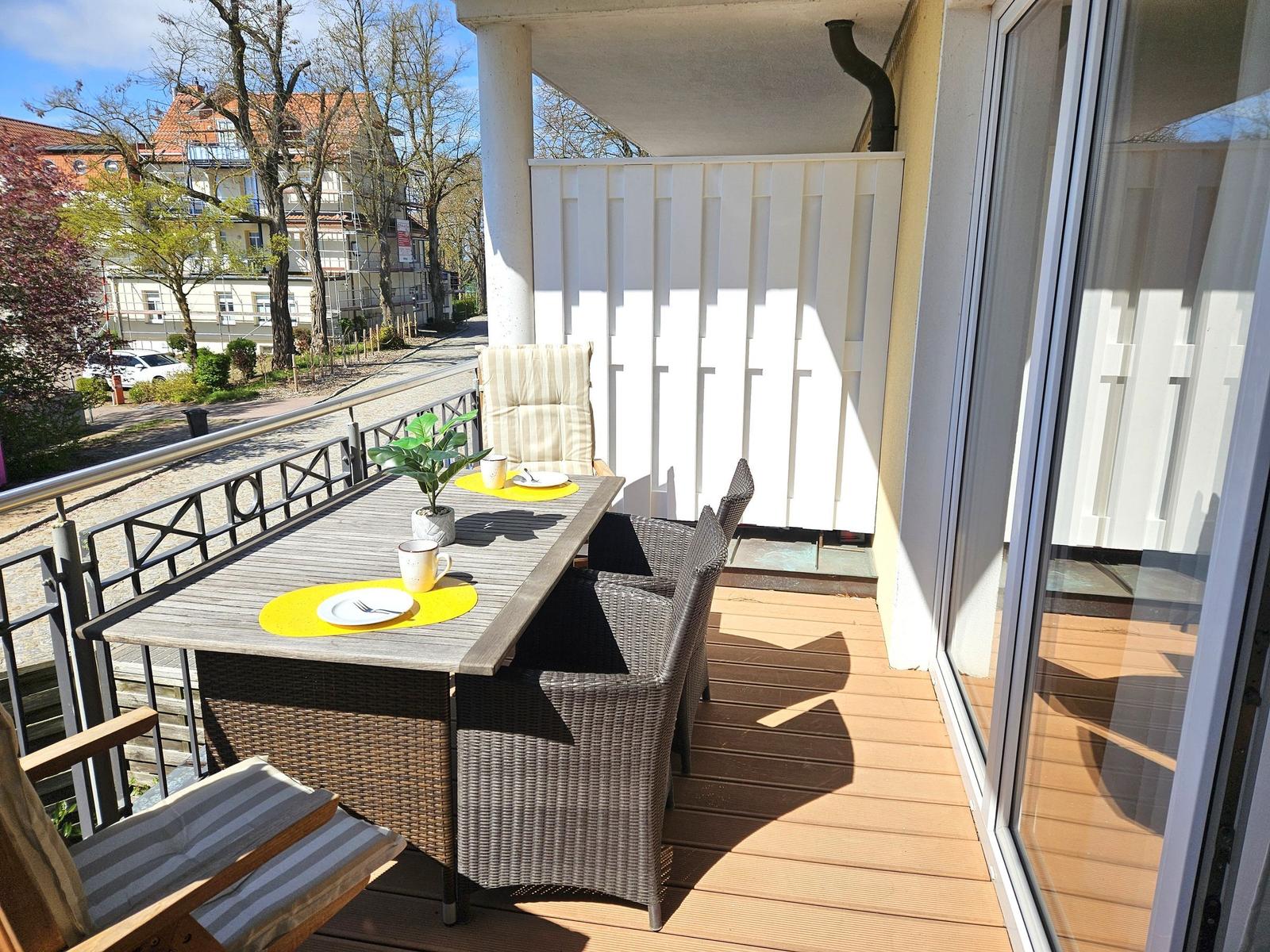 Terrasse mit Tisch, Stühlen und Pflanze. Blick auf Straße und Gebäude.