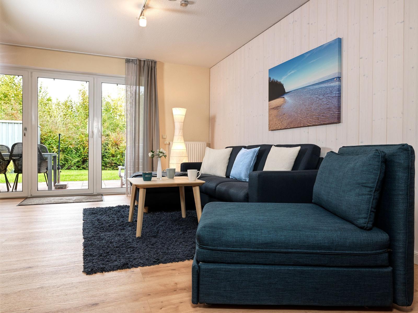 Ein Wohnzimmer mit dunkelblauem Sofa, Holzboden und Blick auf den Garten.