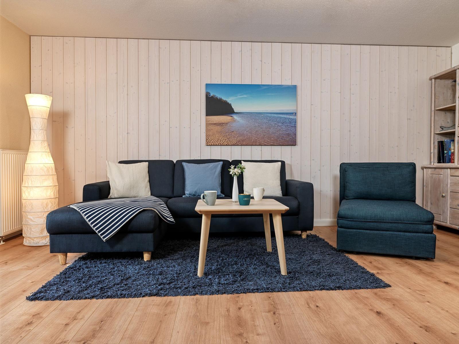 Ein Wohnzimmer mit dunkelblauem Sofa, einem Sessel und einem Holztisch auf einem blauen Teppich.