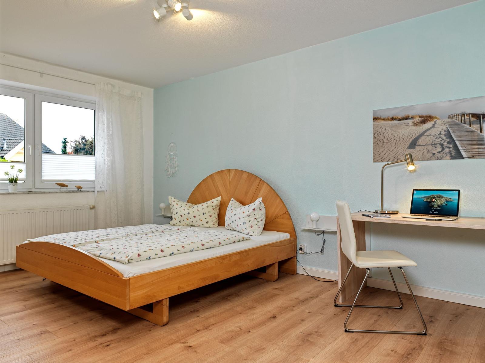 Schlafzimmer mit Bett, Schreibtisch und Fenster. Wandbild und Holzboden.