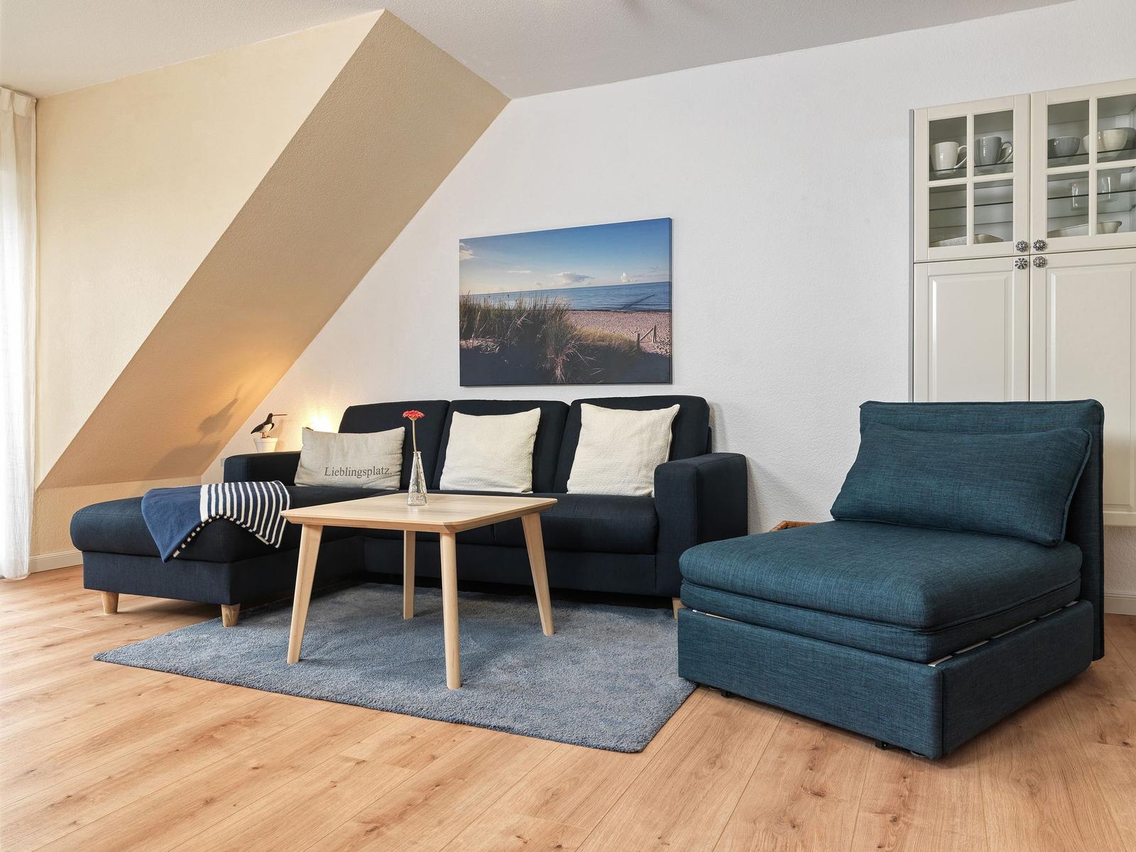 Wohnzimmer mit blauem Sofa, Holztisch und Wandbild. Holzfußboden und weißer Schrank.