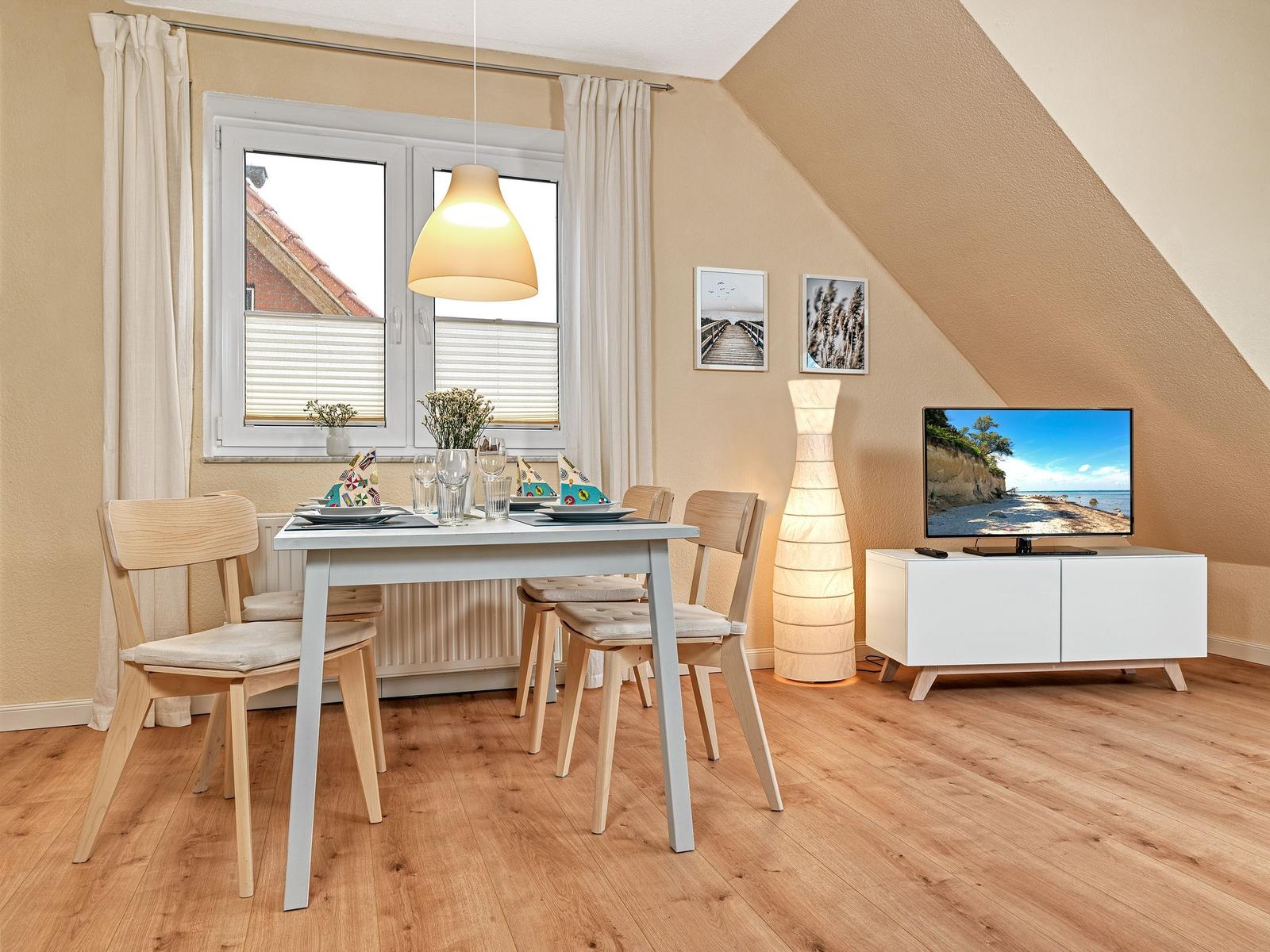 Esszimmer mit Tisch, Stühlen und TV. Holzfußboden und schräge Decke.