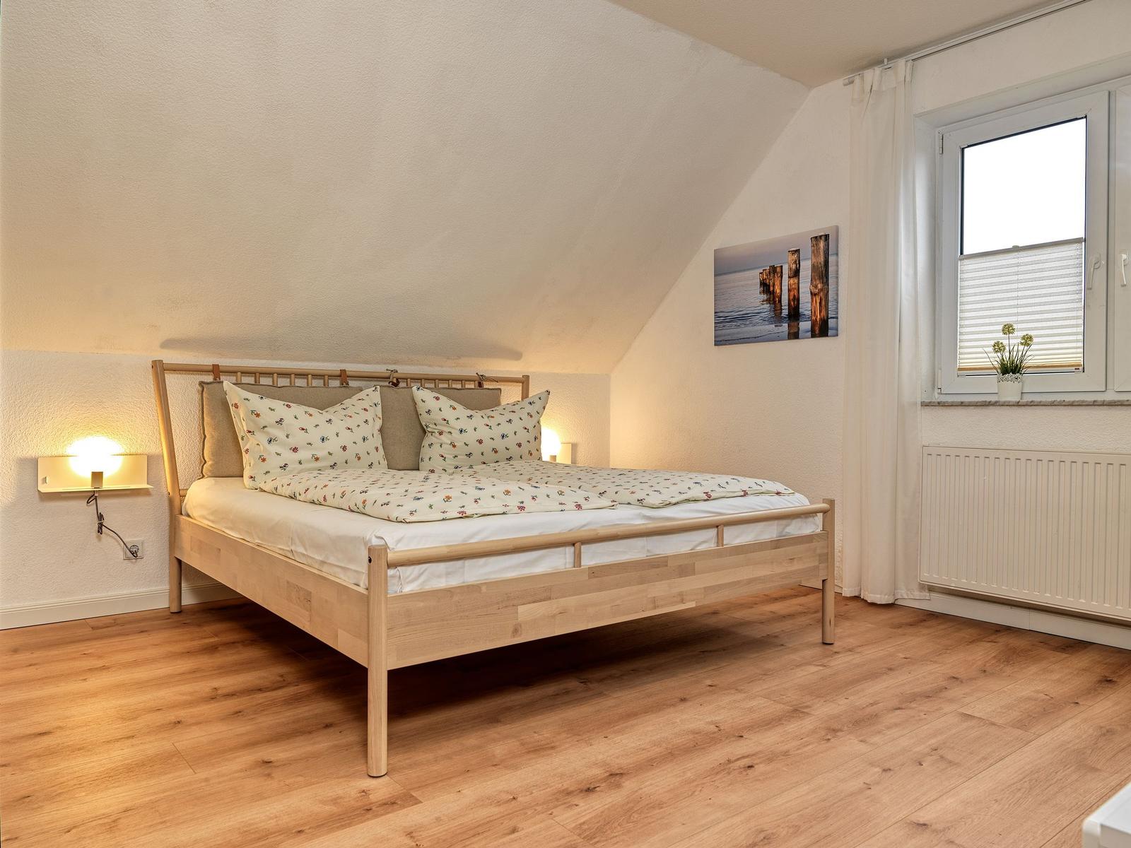 Schlafzimmer mit Dachschrägen, Holzboden und Bett mit gemustertem Bettbezug.