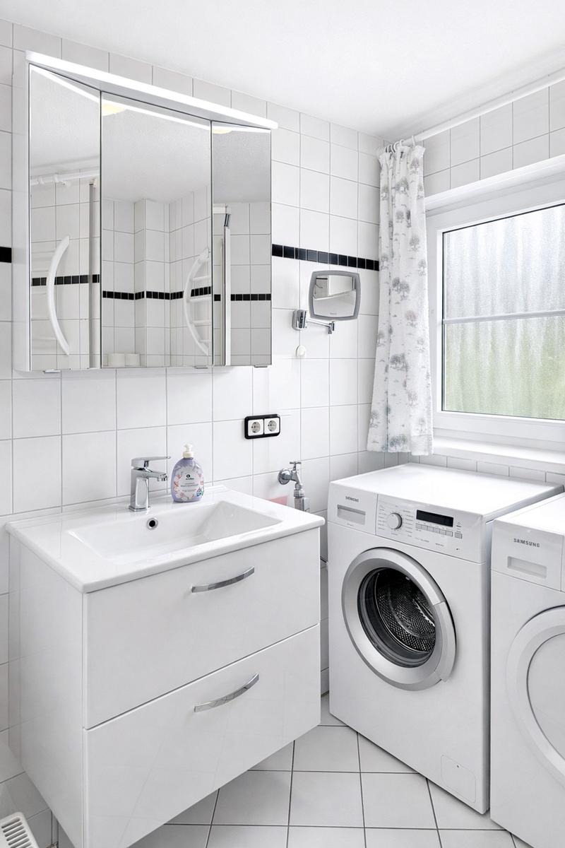 Badezimmer mit Waschmaschine, Spiegelschrank und Fenster mit Vorhang.