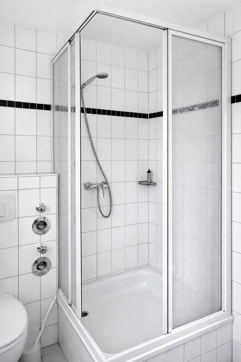 Dusche mit Duschbrause und Glaswand, weiß gefliest mit schwarzer Zierleiste
